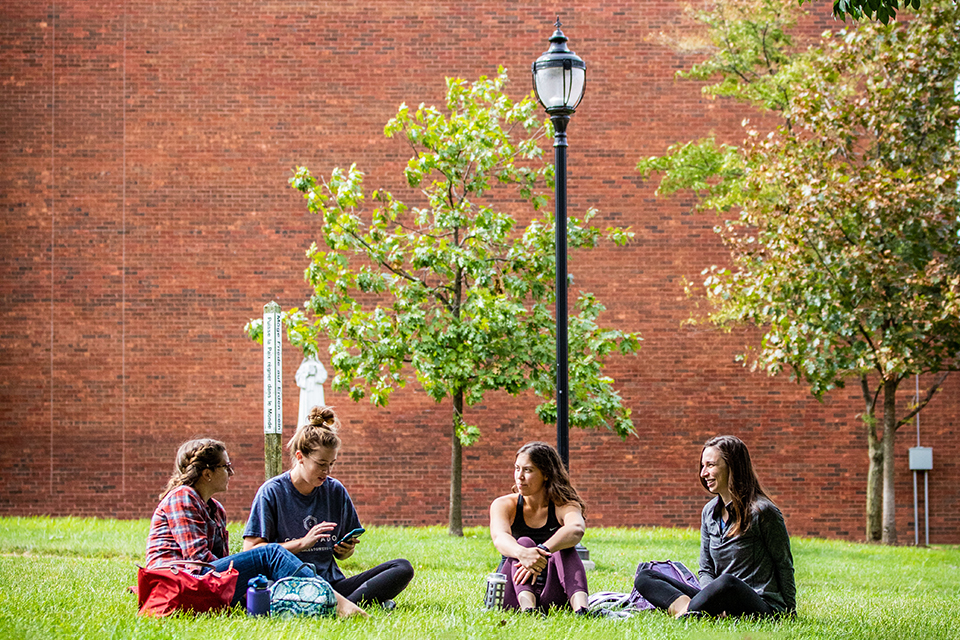 Students sit outside in front of a brick building on a bright, sunny day on SLU's south campus.