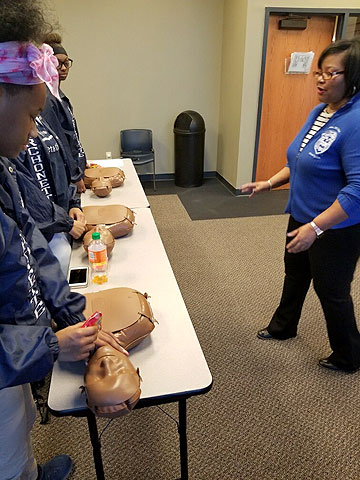 Devita Stallings, Ph.D., RN (right) leads students through a Hands Only CPR Training as the students position themselves above CPR dummies.