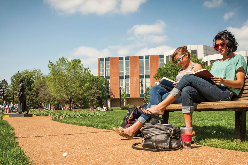 Students study on a bench on the Quad with a view of Ignatius the Pilgrim and Pius Library in the background.