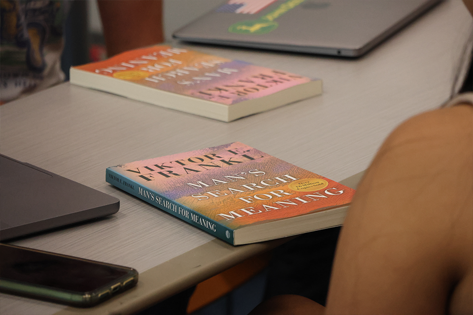 Students' copies of Man's Search for Meaning by Viktor E. Frankl are placed on a table during a class discussion.