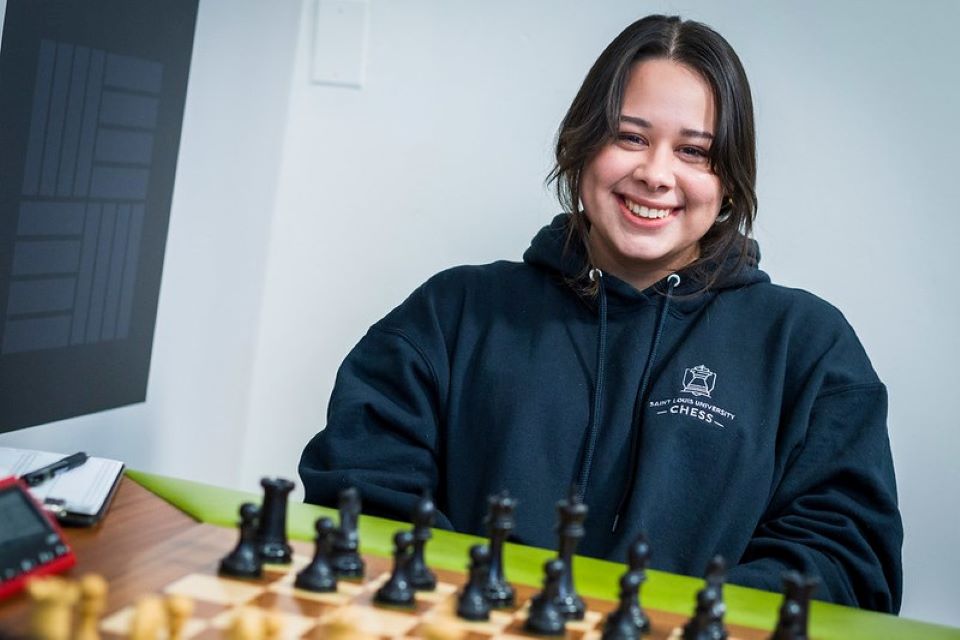 A photo of Thalia Cervantes seated in front of a chess board. She smiles at the camera. 