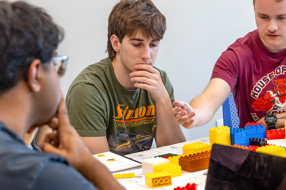 Three male SLU students work together on the UrbanPlan in SLU's Planning the American City class. They sit at a table with a laptop and planning board in front of them.