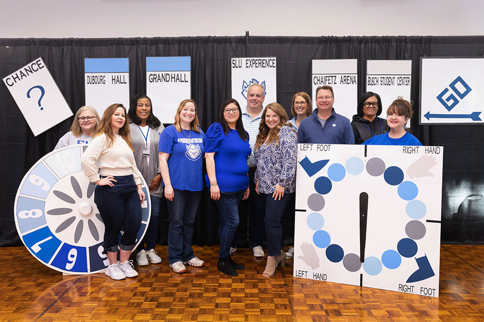 Members of the Billiken Parent and Family Association Eleven BPFA board members standing in front of board-game themed trivia night decorations.