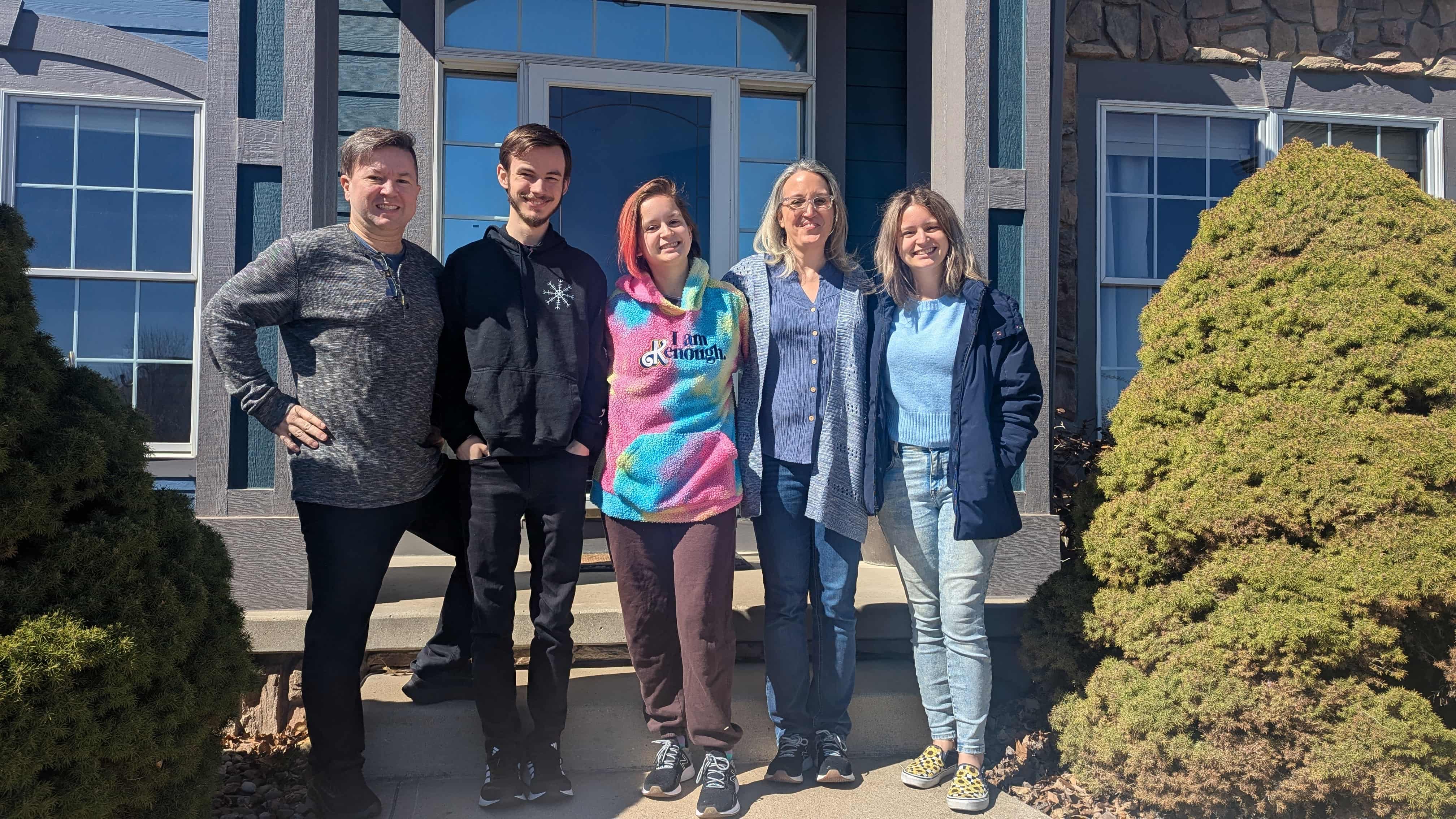 Five people stand in front of a house in a line.