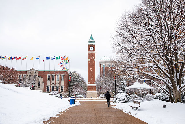 A person is seen from behind as they walk along a snowy campus toward the clock tower and center for global citizenship