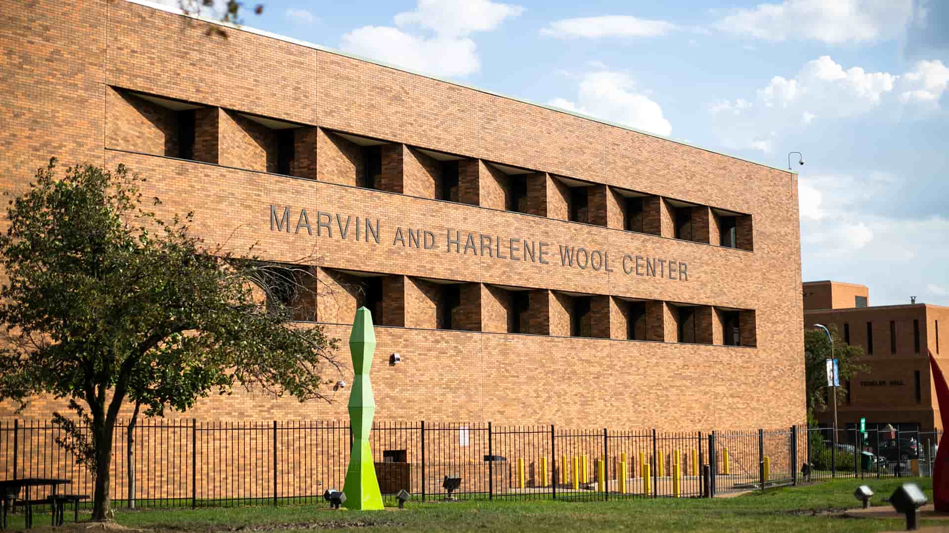 A view of the Wool Center from the Northwest looking toward the Southwest at the Western facing facade of the brick building on the other side of a sculpture park. 