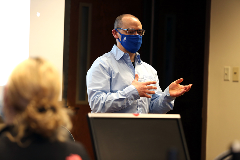 Travis Loux, Ph.D. teaching a biostatistics class. He stands at the front of a classroom, wearing a blue shirt and a blue mask.