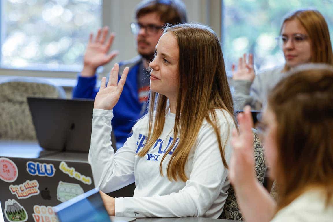 A SLU student raises their hand while sitting in a classroom.