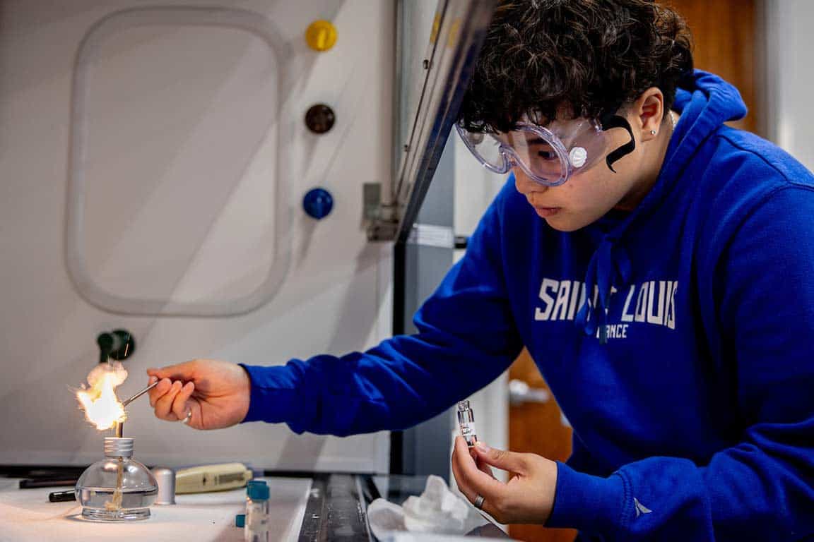 A forensics student works with a chemical in a fume hood.