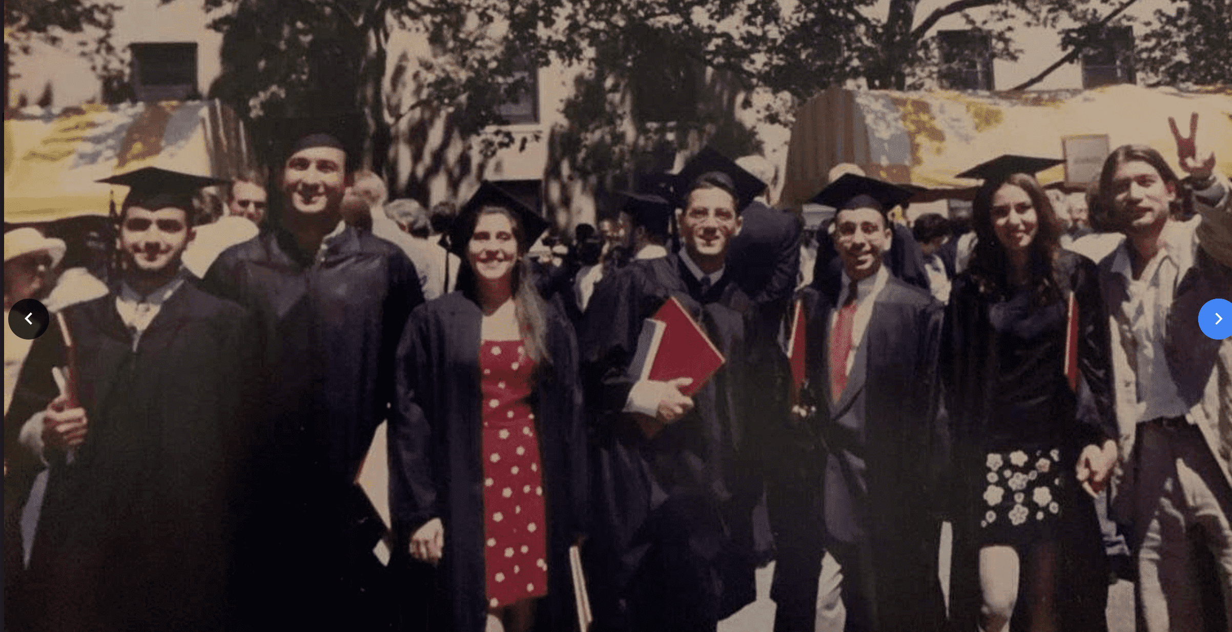 A group of graduates in caps and gowns smile at the camera.