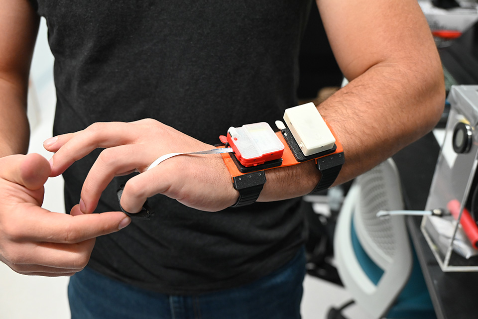 An arm wearing a haptic device, consisting of two rectangles mounted on straps attached to the wrist.