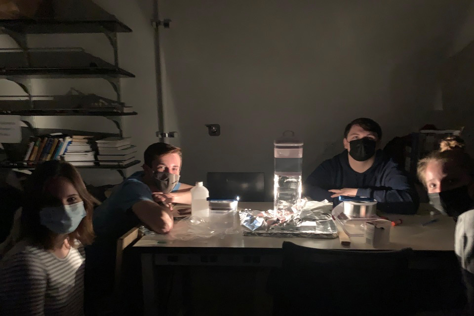 Four students sitting at a table, working on a cloud chamber