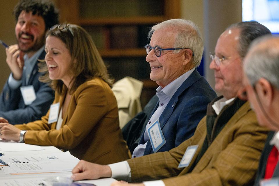 A row of people sit at a table with papers in front of them smiling and laughing.