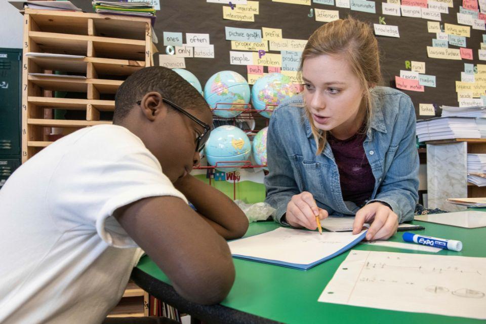 College student teaching an elementary school student in an elementary school classroom