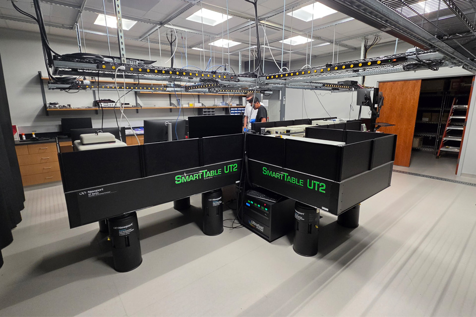 A lab space shows large black tables and various quantum-related equipment.