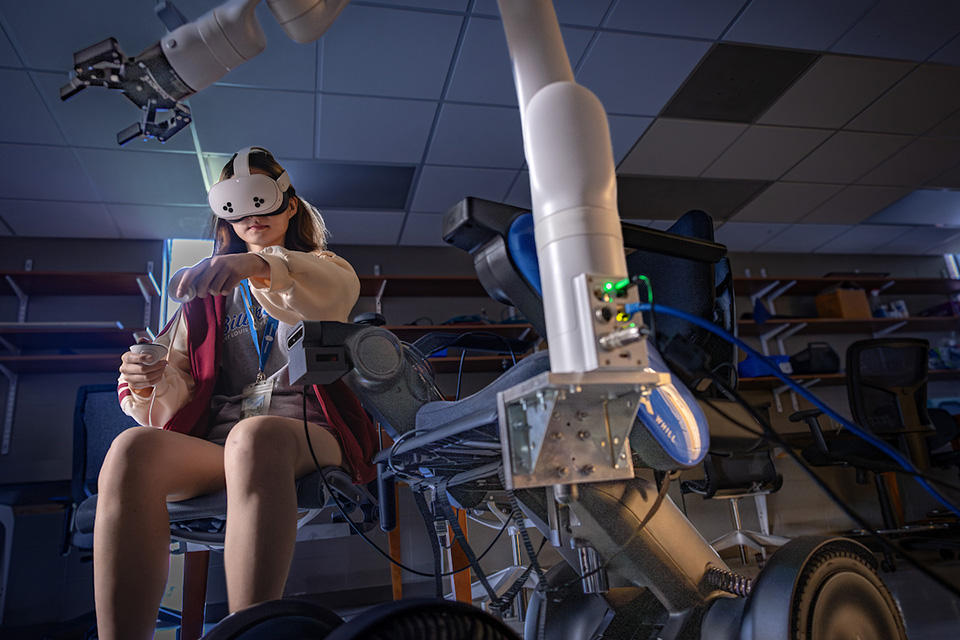 Wheelarm Demonstration A student sits in a seat with a robotic arm while wearing VR glasses.