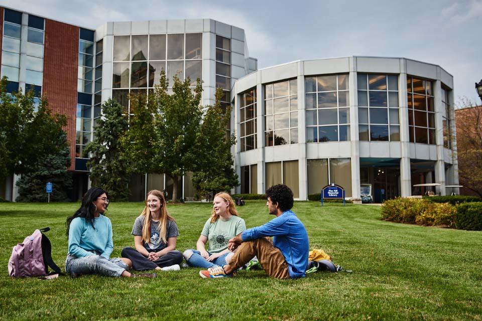 Students and library. Students sit on the grass outside of the library.