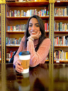 Shabnam Nejat  posing with coffee at a table in front of a wall of books