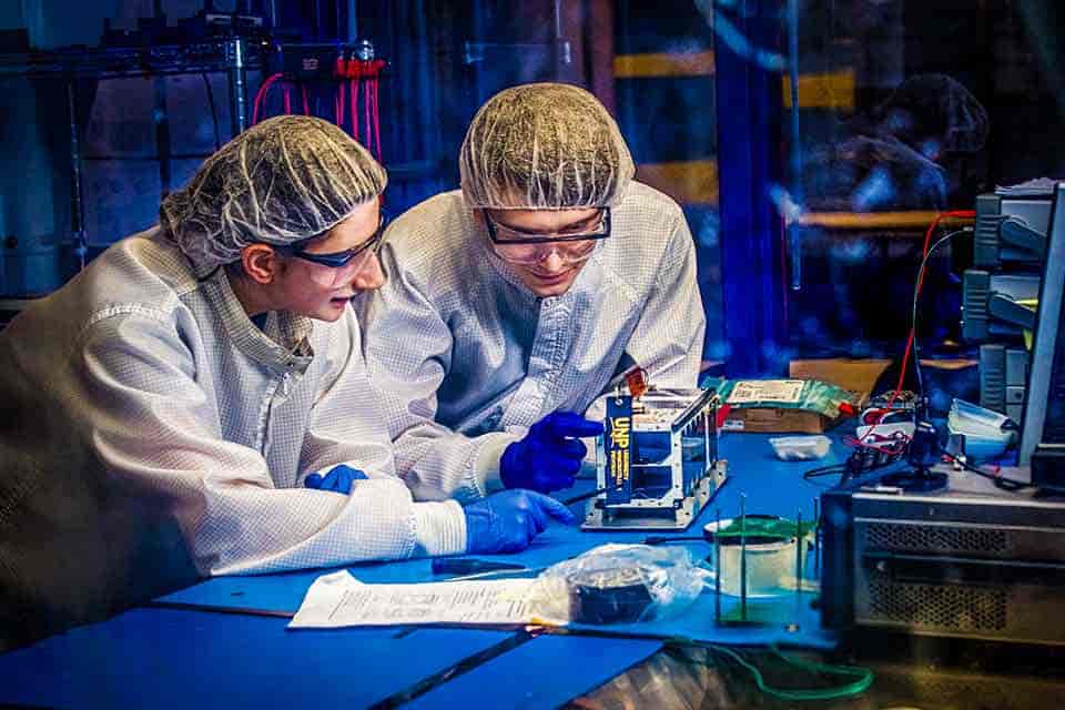 Two SLU students examine a mechanical part in a lab setting