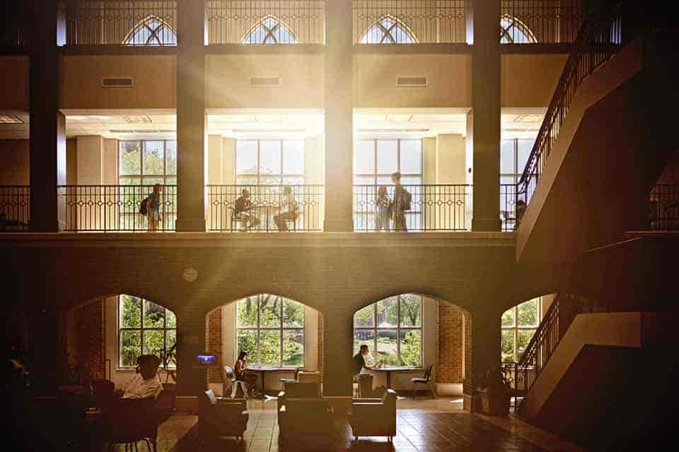 Students walk past a window in SLU's Cook Hall as sunlight pours through.