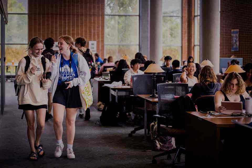 Visiont and Strategy Students walk in Pius Library as other students study at computers in the background.