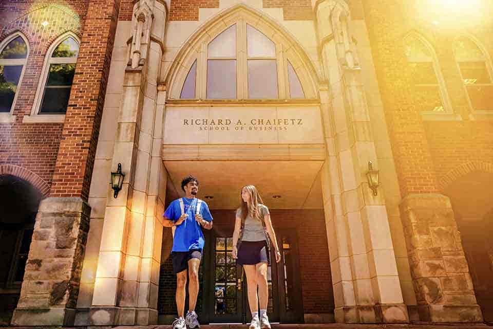 Why Now Two SLU students exit Cook Hall through an archway with "Chaifetz School of Business" printed above it.