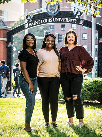 Three female students from the First Period Kit Project stand under an arch at SLU.