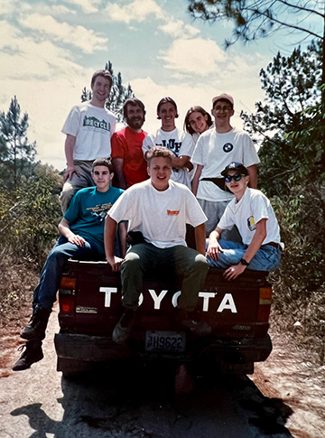 A group of eight teen boys stand and sit in the bed of a Toyota pickup truck.
