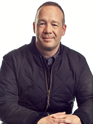 Profile shot of Tim Bantle, CEO of Eddie Bauer. Bantle has close-cropped hair and wears a dark zip-up quilted jacket. 