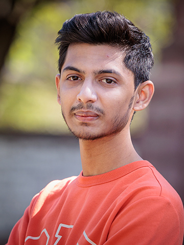 A profile photo of a male graduate student from India, with short dark hair and wearing an orange t-shirt