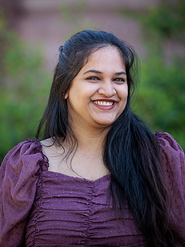A profile photo of a female graduate student from India with long dark hair and wearing a burgundy top