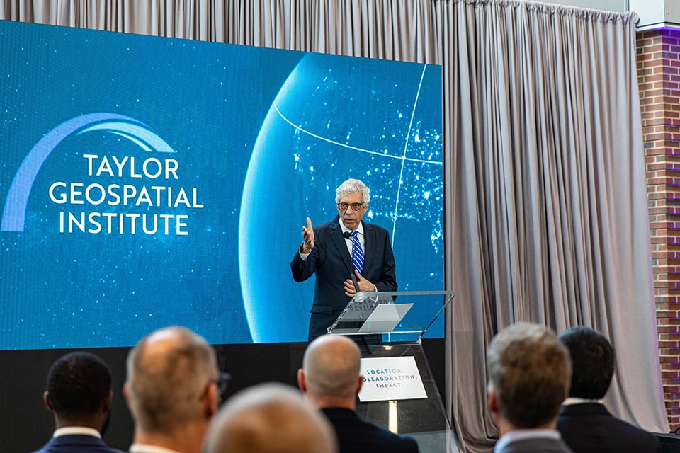 Dr. Fred P. Pestello speaks to an audience during the launch of the new geospatial insitute in front of sign reading Taylor Geospatial Institute