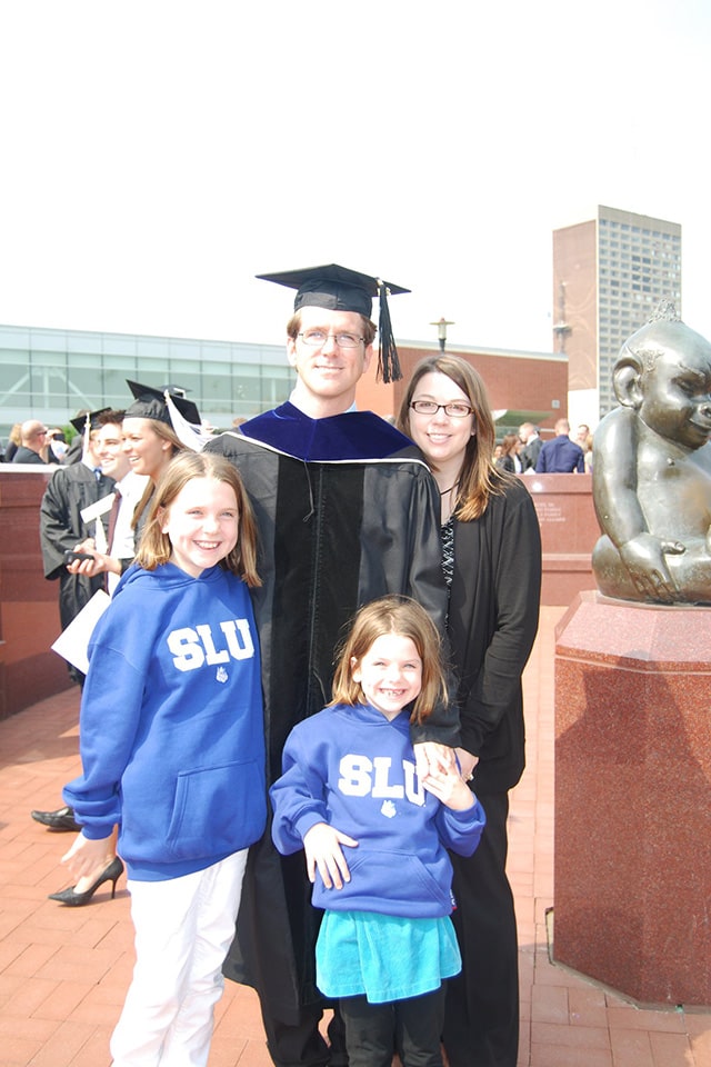 Sowell wears a graduation cap and gown while posing with his family at SLU commencement