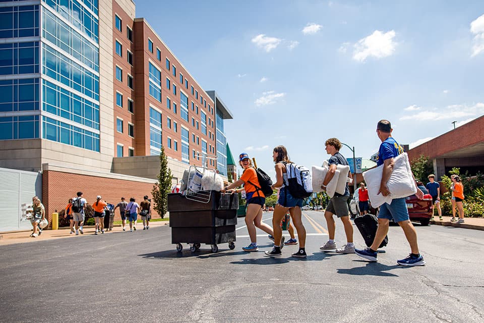 A member of Oriflamme helps a new student and her family carry her belongings across the street during move-in.