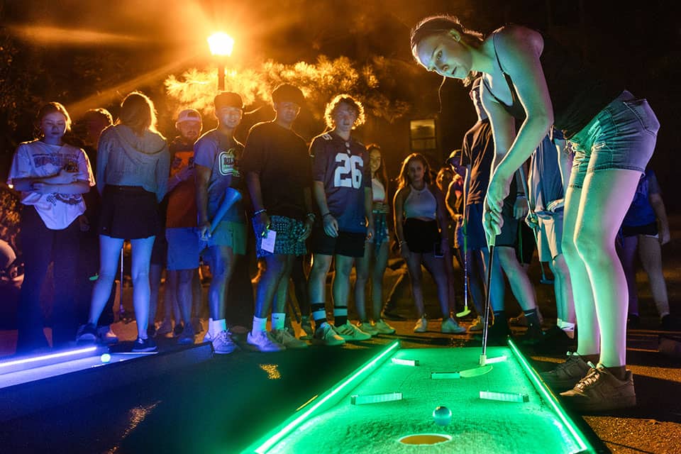 A student plays mini-golf on an illuminated golf course during the annual move-in street party.
