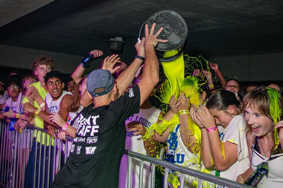 A member of the SLU paint staff pours neon yellow paint on the crowd.